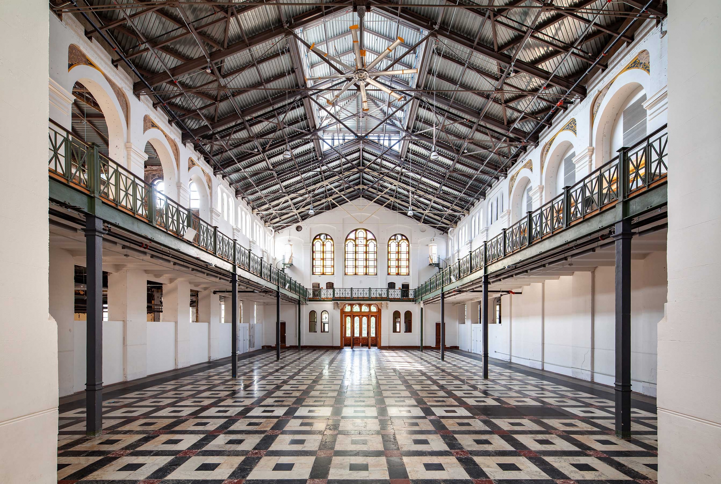 Hall with large windows at one end, a balcony on the sides, and a tiled floor