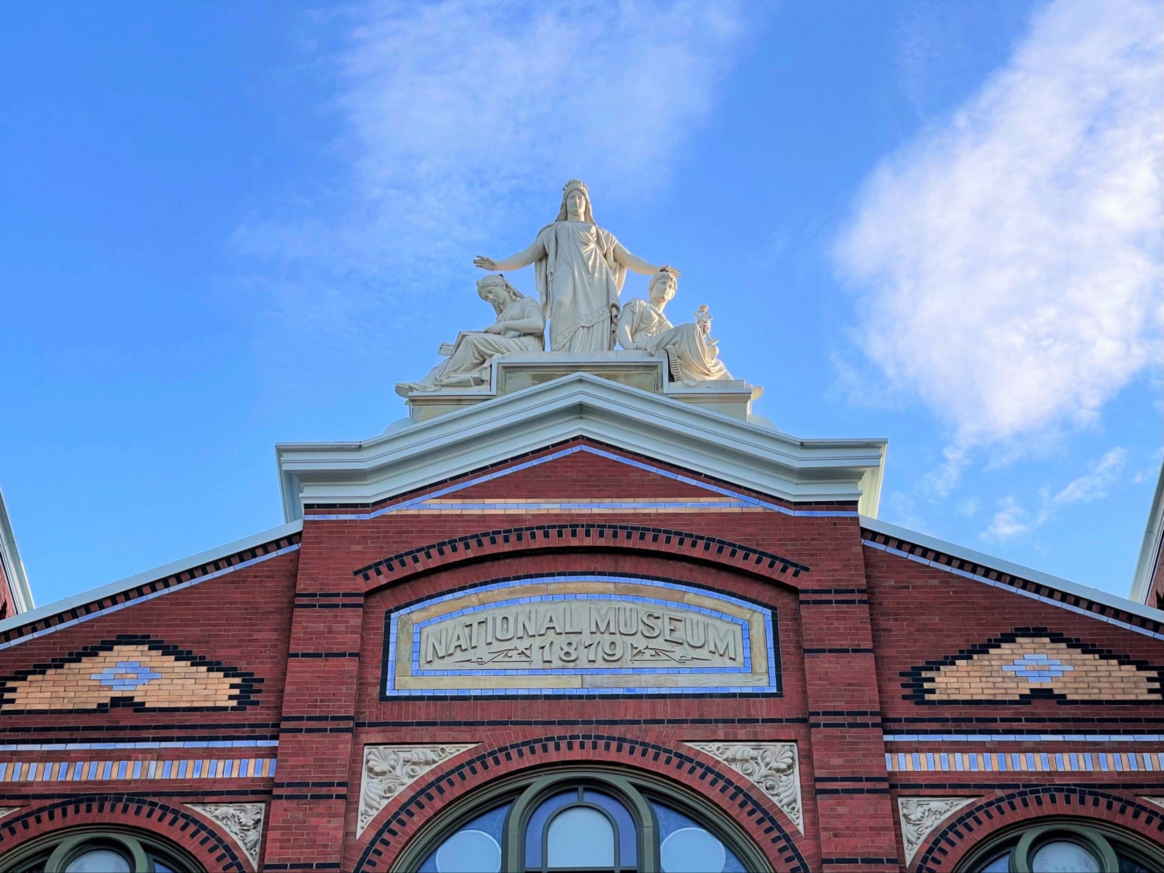 Detail of the roof of a red brick building, with a statue of three figures